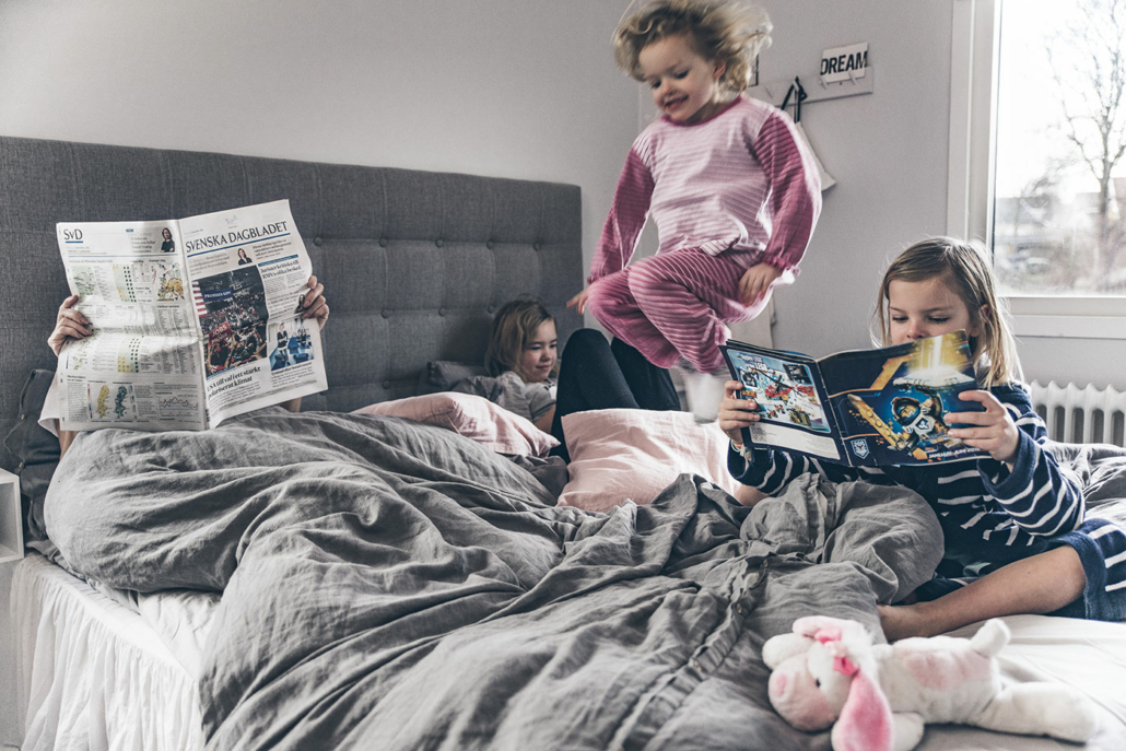 familjemys i sängen med barn som surfar, läser och hoppar i sängen där pappa läser svenskan