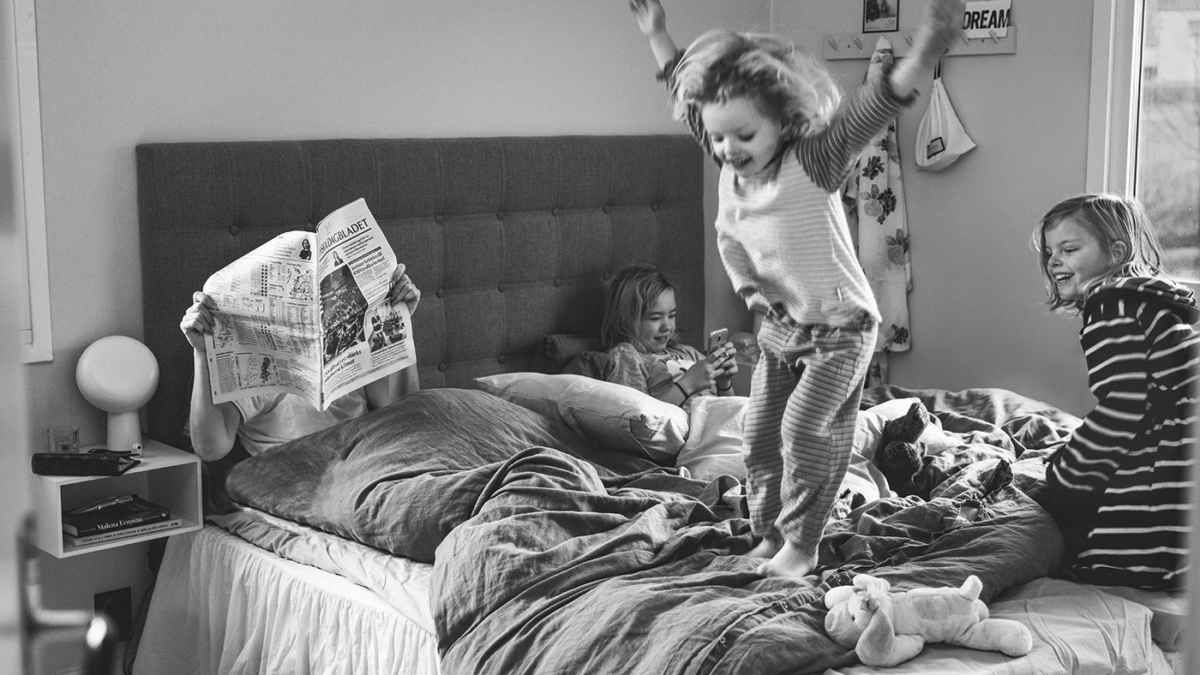 Flickan hoppar i sängen medan syskonen leker och surfar och pappan läser tidningen