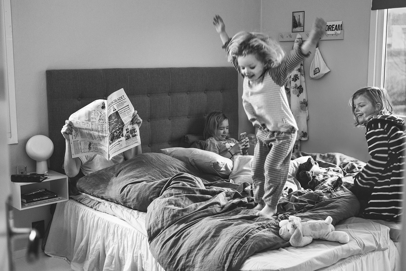 Flickan hoppar i sängen medan syskonen leker och surfar och pappan läser tidningen