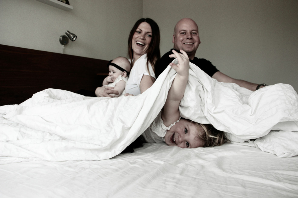 familjen i sängen där dottern lekfullt tittar fram från under täcket
