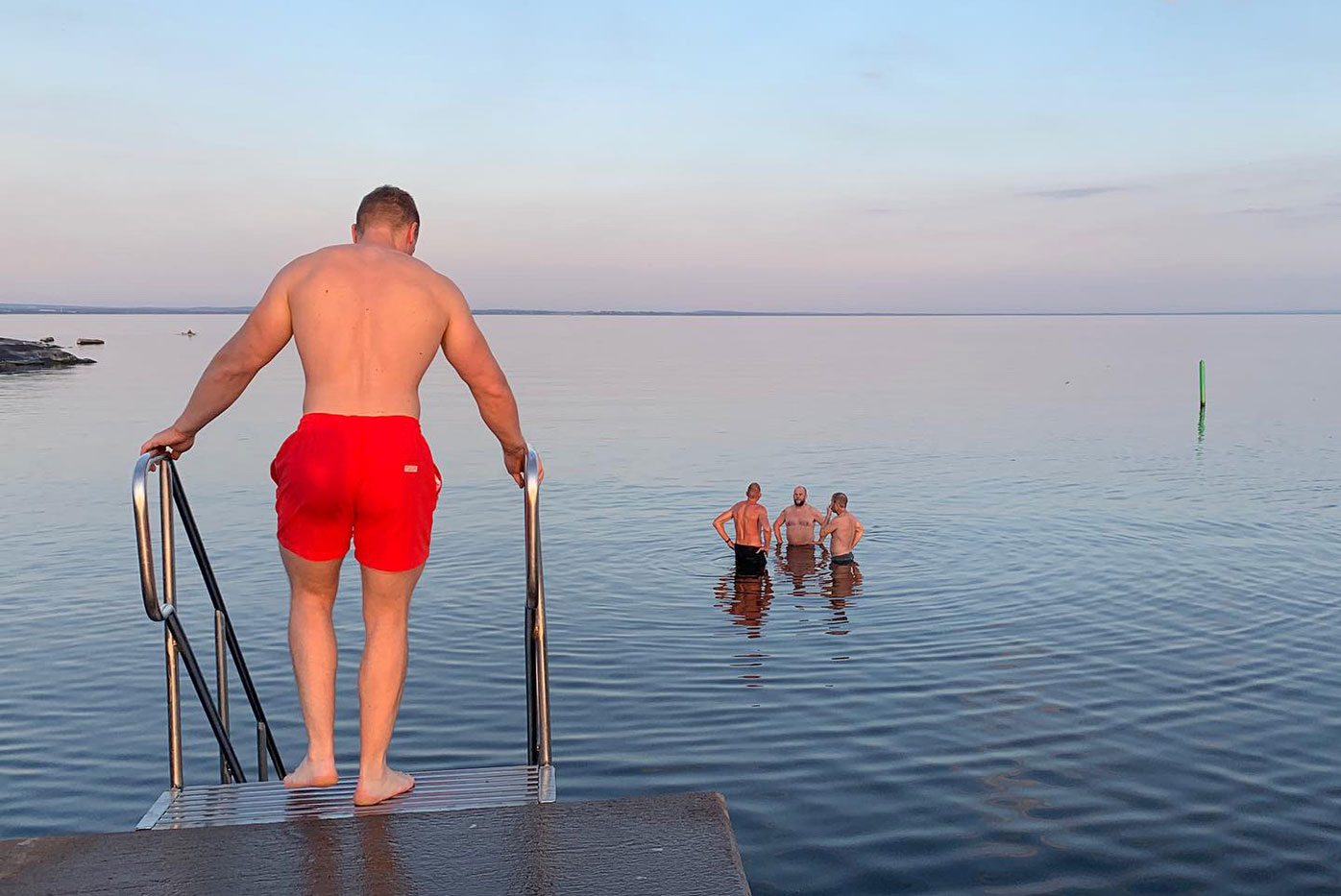 Killar badar från brygga i Grötvik i spegelblankt hav